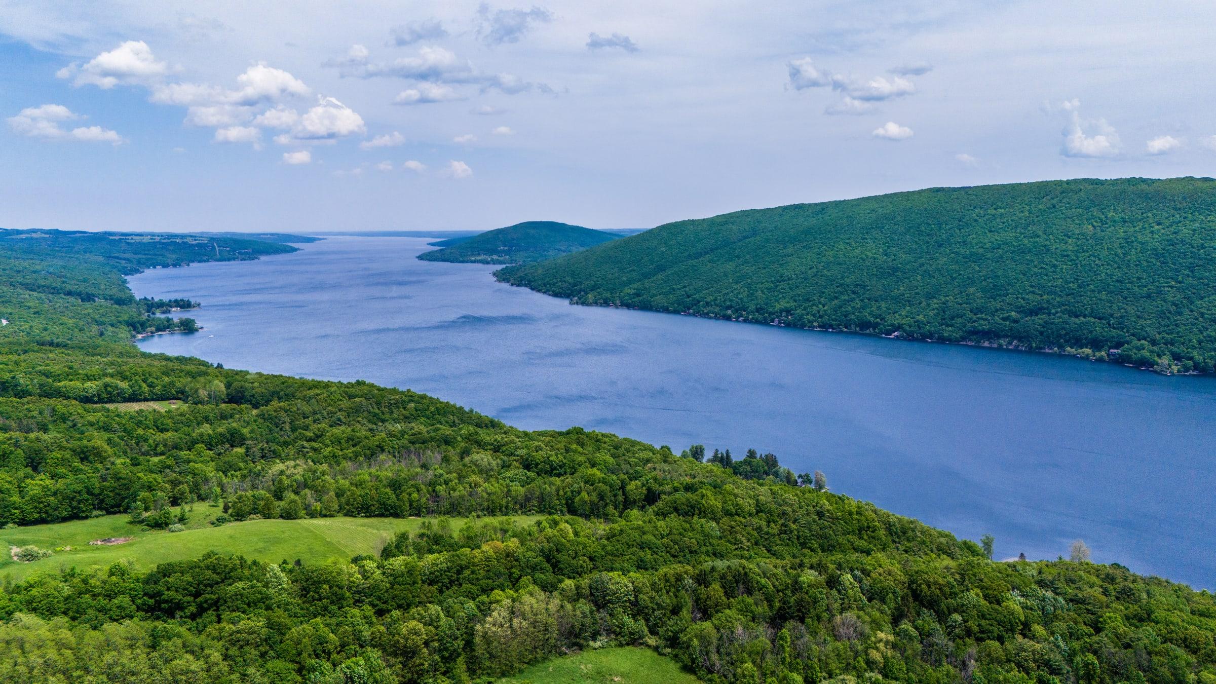 Wide aerial view of Canandaigua Lake running between densely wooded green hills.